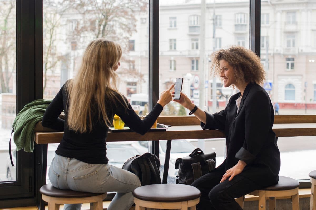 Two friends sharing a link on a phone at a café